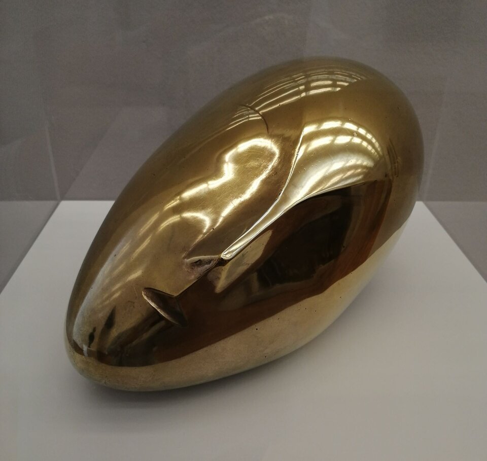 Ilustracja przedstawia rzeźbę „Śpiąca Muza II” autorstwa Constantina Brâncușiego. Jest to forma zbliżona do kształtu jaja z lekko zarysowanym nosem i ustami. Faktura jest błyszcząca i  idealnie gładka. 