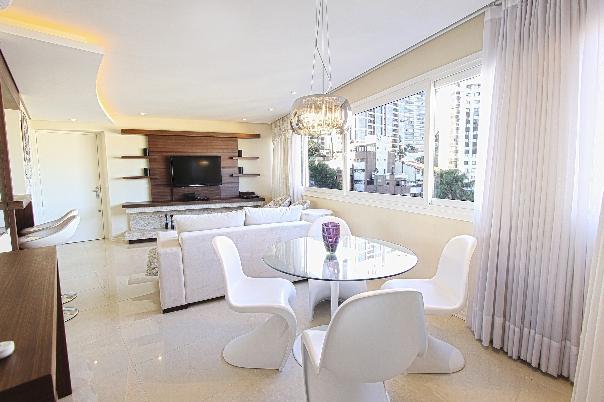 Na zdjęciu znajduje się wnętrze salonu ze szklanym okrągłym stołem i czterema białymi krzesłami.