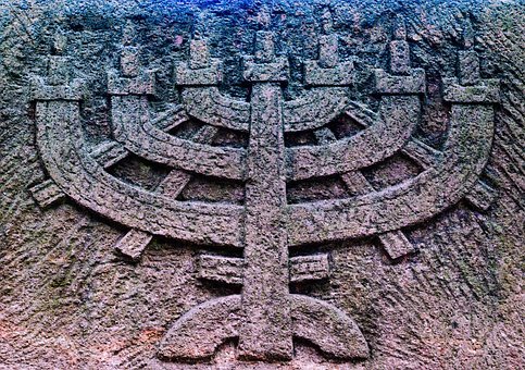 Kolorowa fotografia przedstawia kamienną płaskorzeźbę w kształcie menory, siedmioramiennego świecznika.