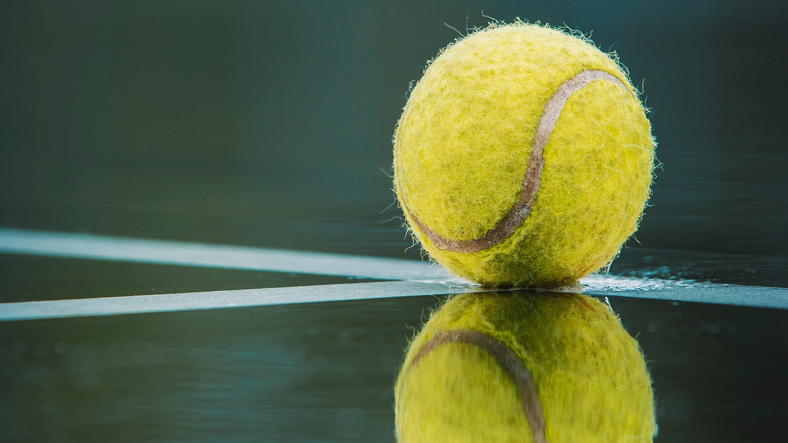 Zdjęcie przedstawia żółtą piłkę do tenisa ziemnego leżącą na korcie.