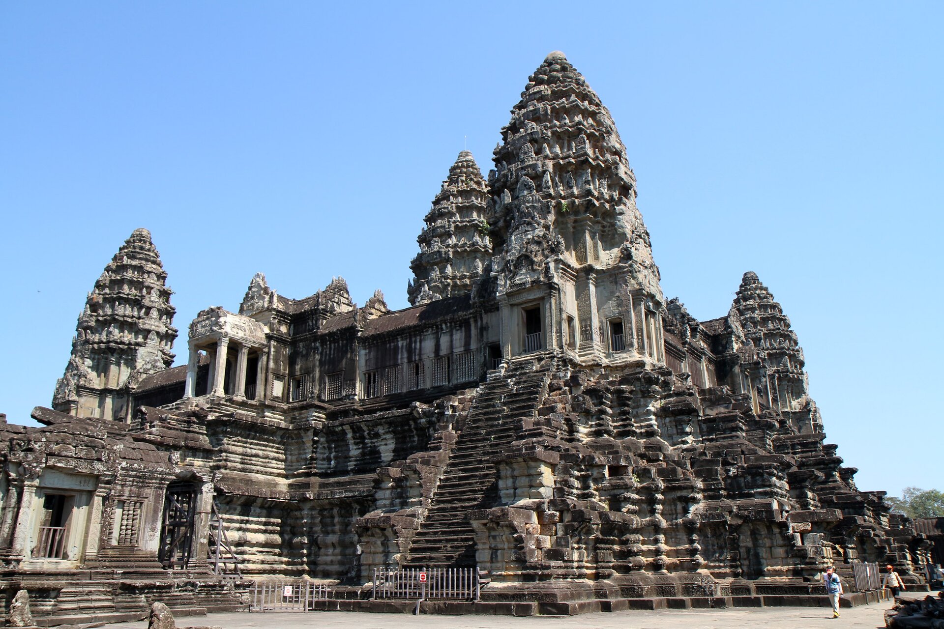 Zdjęcie przedstawia Angkor Wat w Kambodży. Jest ono największą świątynią buddyjską na świecie. Jest w całości zbudowane z kamienia. Ma okrągłe wysokie kopuły oraz schody. Widać ludzi spacerujących przed świątynią.