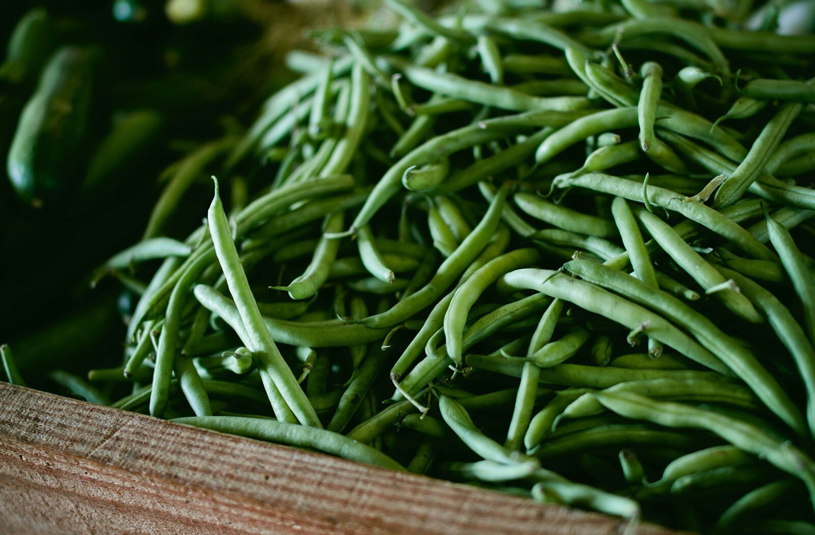 Zdjęcie przedstawia skrzynkę pełną zielonej fasolki. 