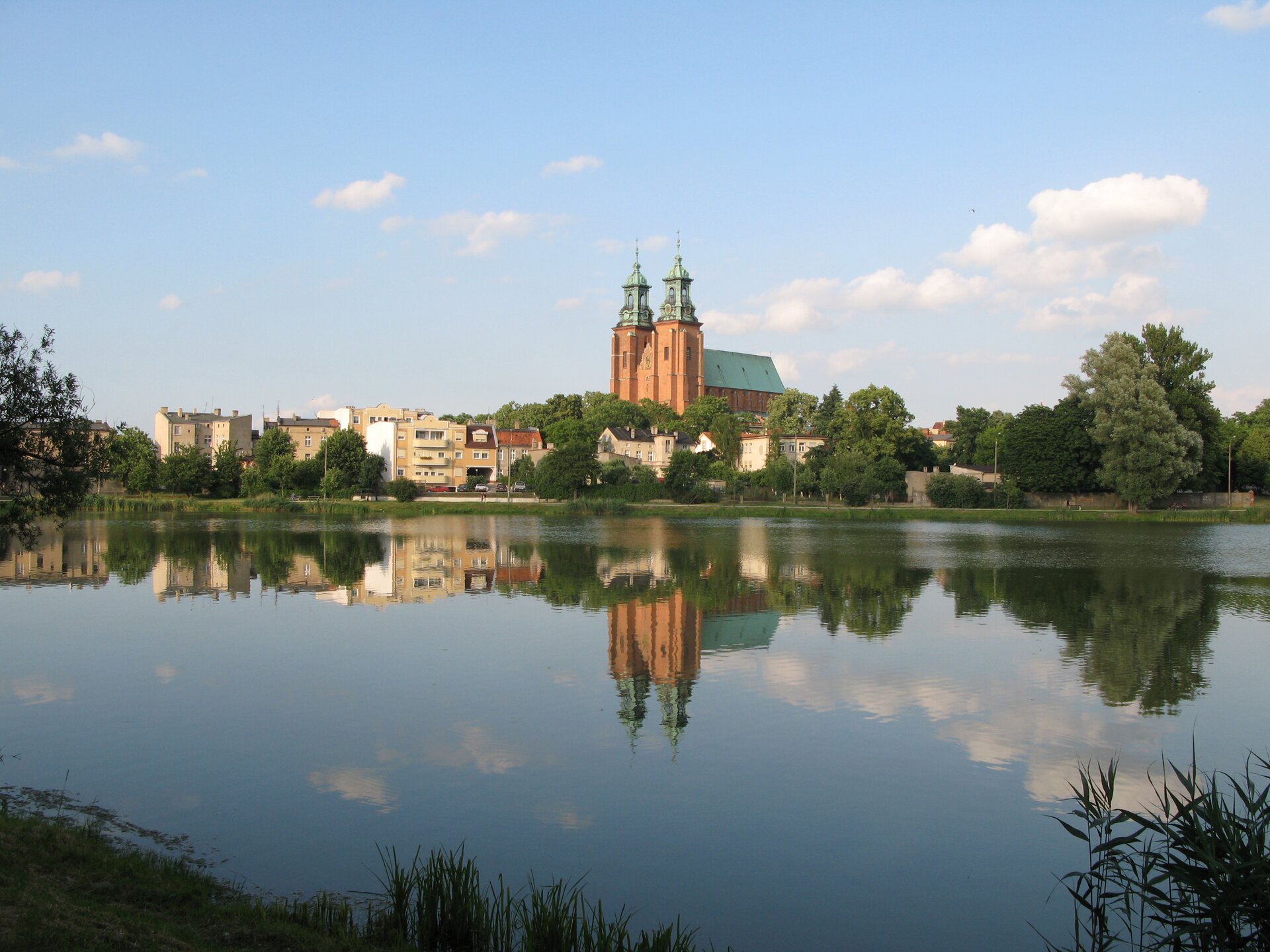 Na zdjęciu wysoki kościół z dwoma wieżami i zabudowa miejska nad brzegiem rzeki.