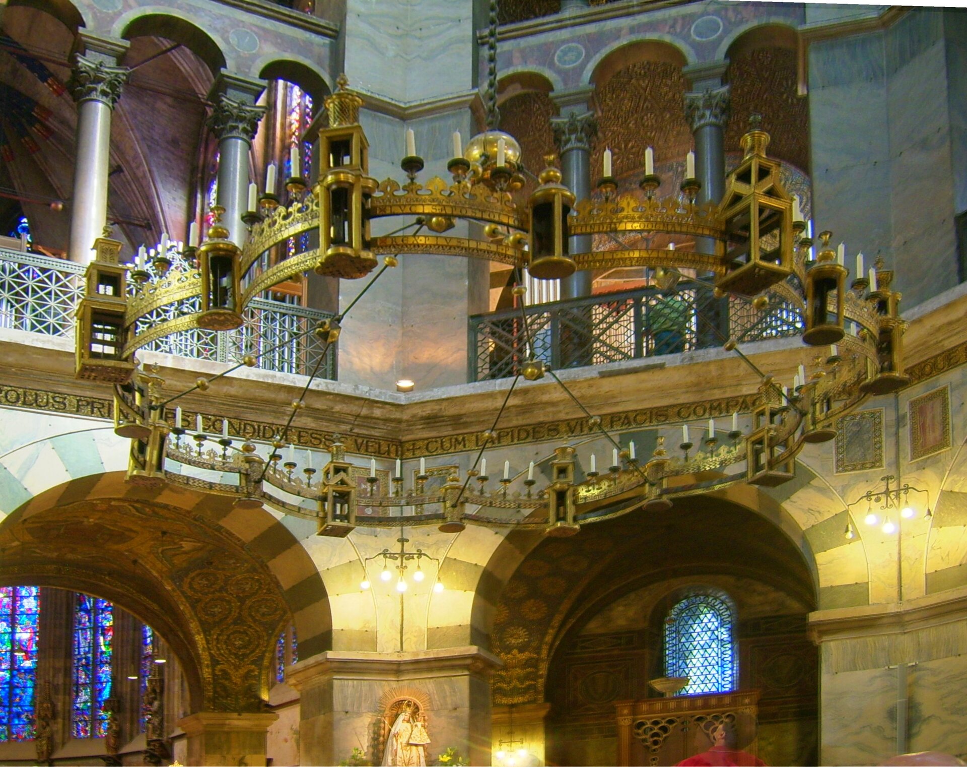 Zdjęcie przedstawia duży świecznik kolisty, który znajduje się pod kopułą dachu kaplicy, na którym umieszczonych jest 48 świec. Wykonany jest z pozłacanej miedzi. Przymocowany jest na łańcuchu na środku pod dachem. Świecznik składa się z 8 segmentów okręgu i jest tym samym dostosowany do ośmiokątnej formy kaplicy pałacu. Obręcz świecznika wygląda jak mur miejski, który zawiera 8 dużych i 8 małych latarni. 