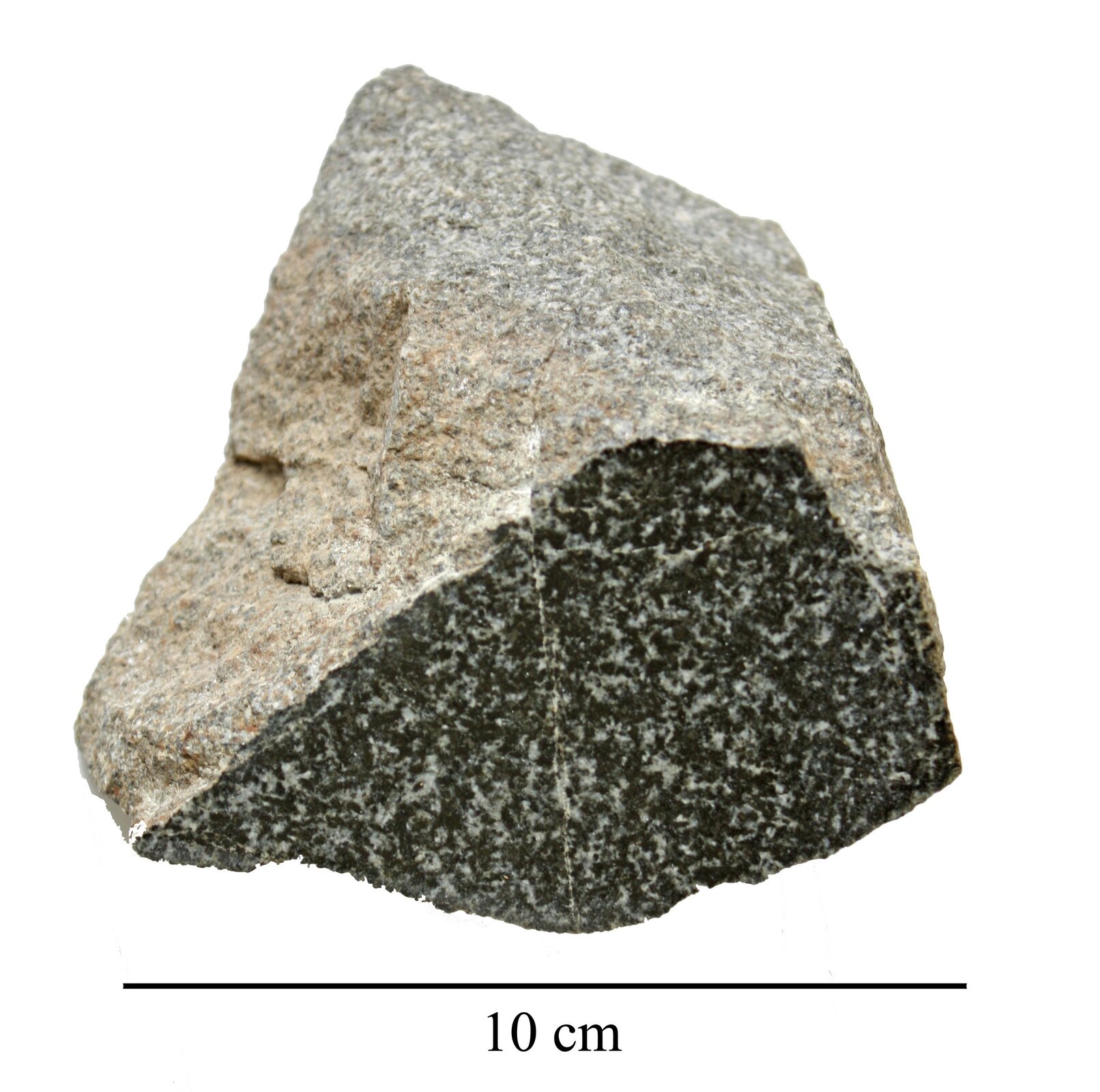 Zdjęcie przedstawia diabaz. Ma on kształt zbliżony do trójkąta. Jego powierzchnia jest chropowata. Górna część ma barwę jasną natomiast dolna czarną z białymi domieszkami. Długość skały wynosi 10 centymetrów.
