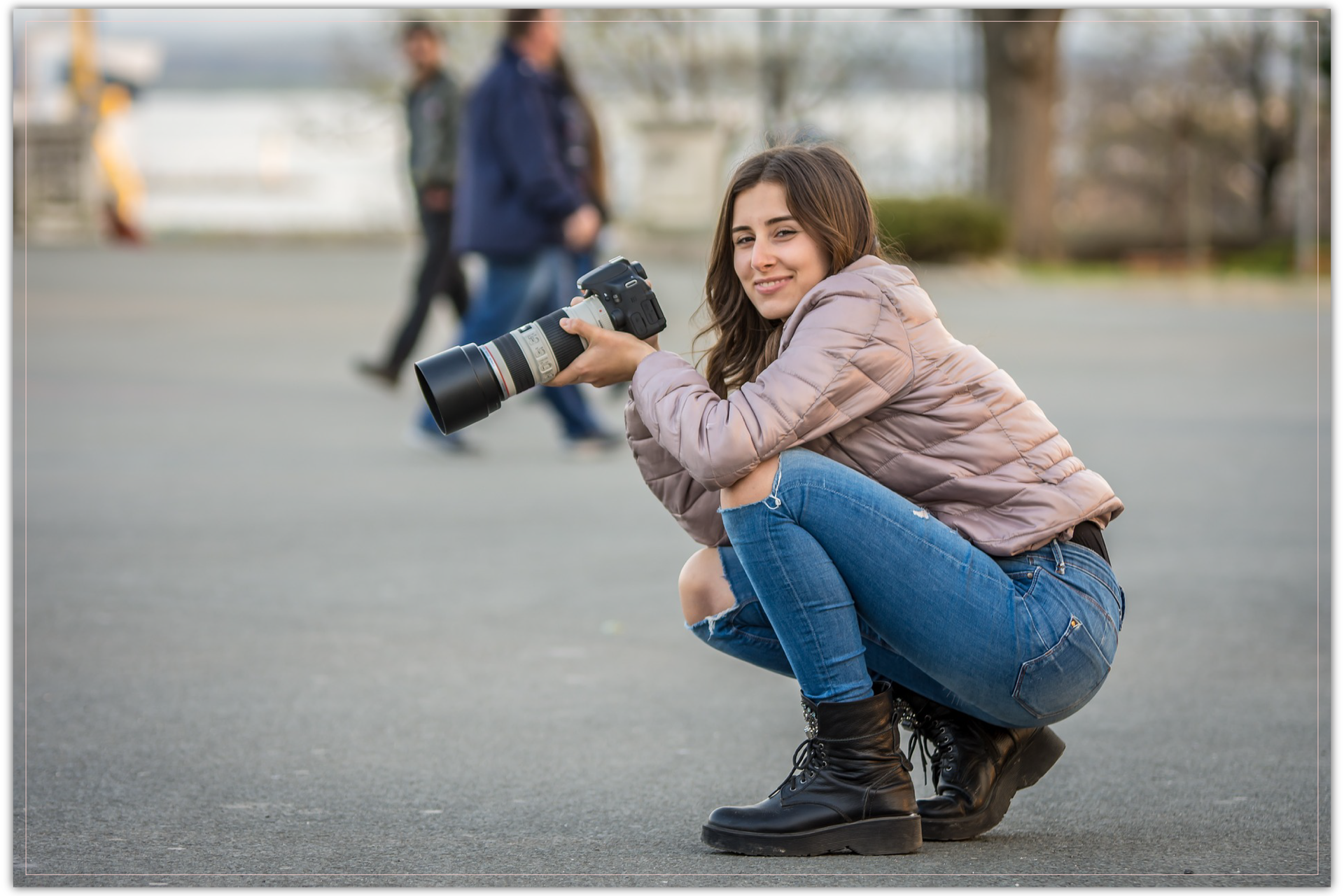 Zdjęcie przedstawia dziewczynę kucającą z aparatem fotograficznym w ręce.