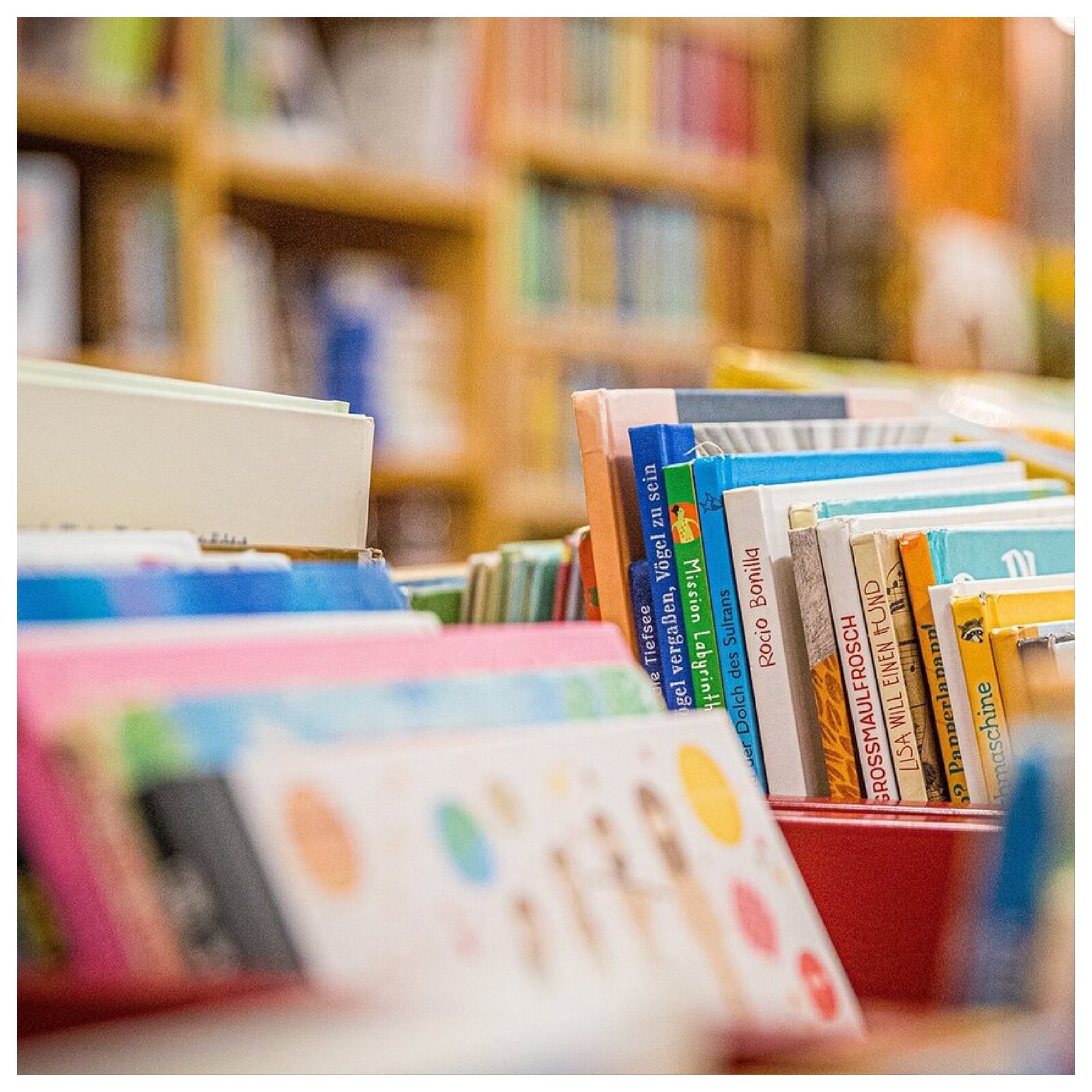 Zdjęcie przedstawia pojemniki z książkami. W tle widoczne są regały pełne książek.