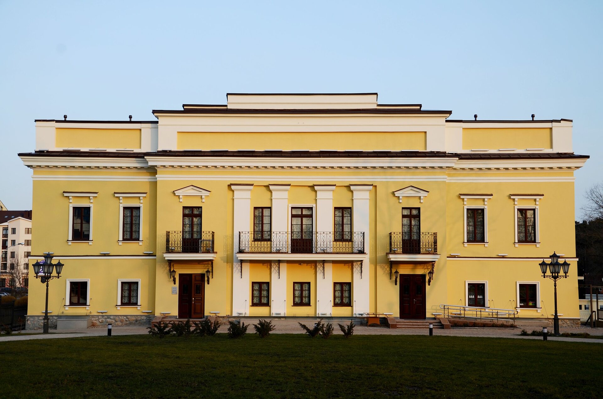 Fotografia fasady pałacu w kolorze żółtym. Ozdobne pilastry w centralnej części fasady, prosta bryła budynku.