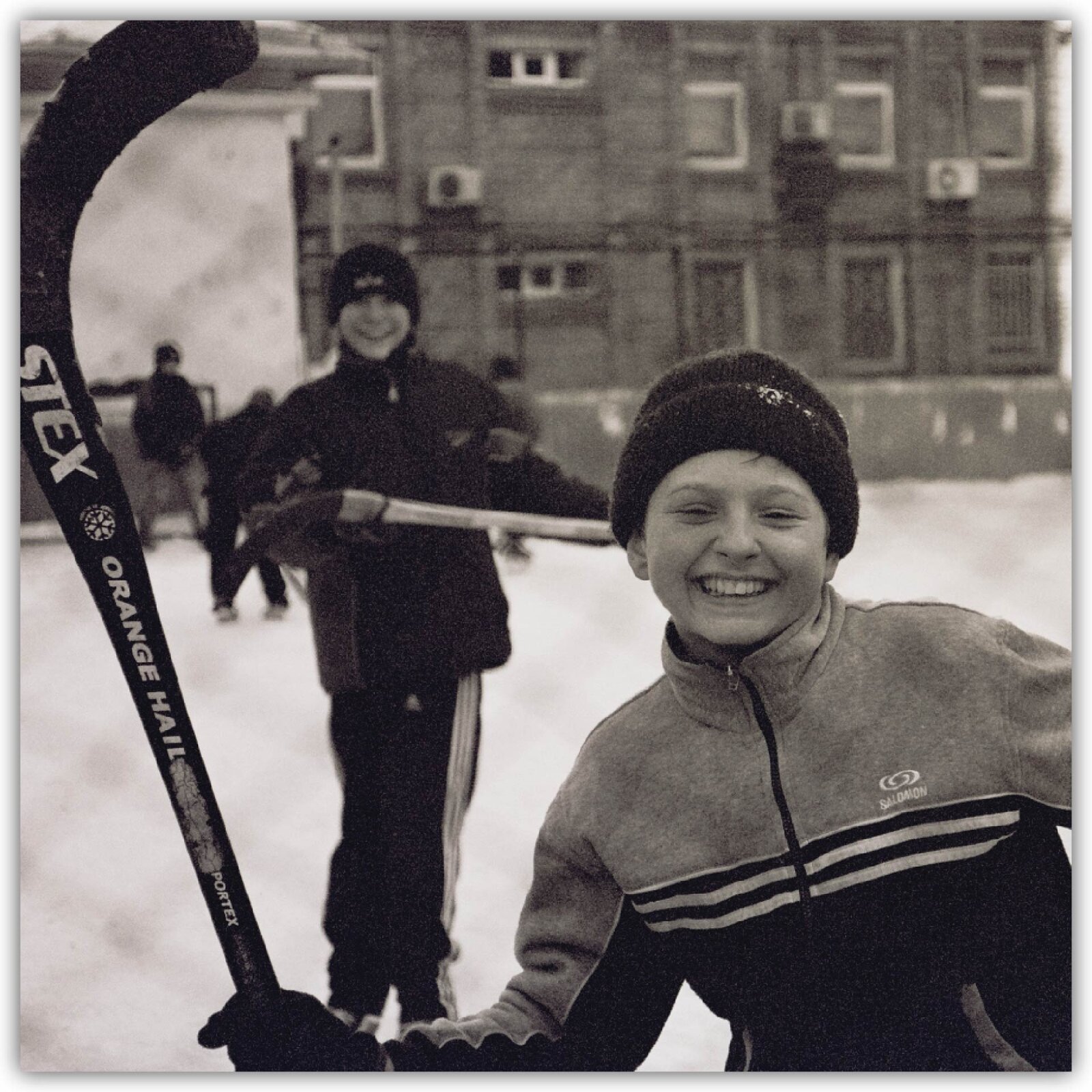 Ilustracja przedstawia uśmiechniętych chłopców na lodzie z kijami do hokeja.