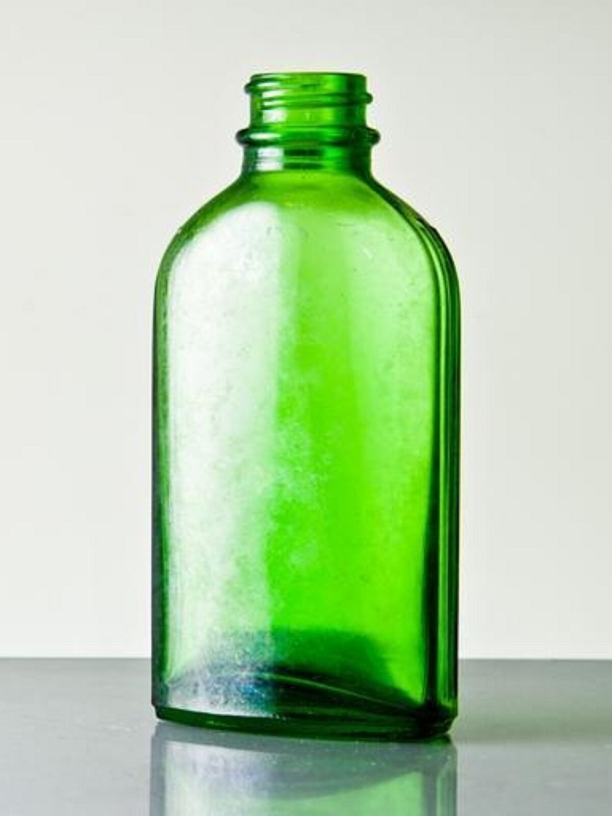 Grafika przedstawia zielone naczynie szklane w formie bocznie spłaszczonej butelki zakręcanej.
