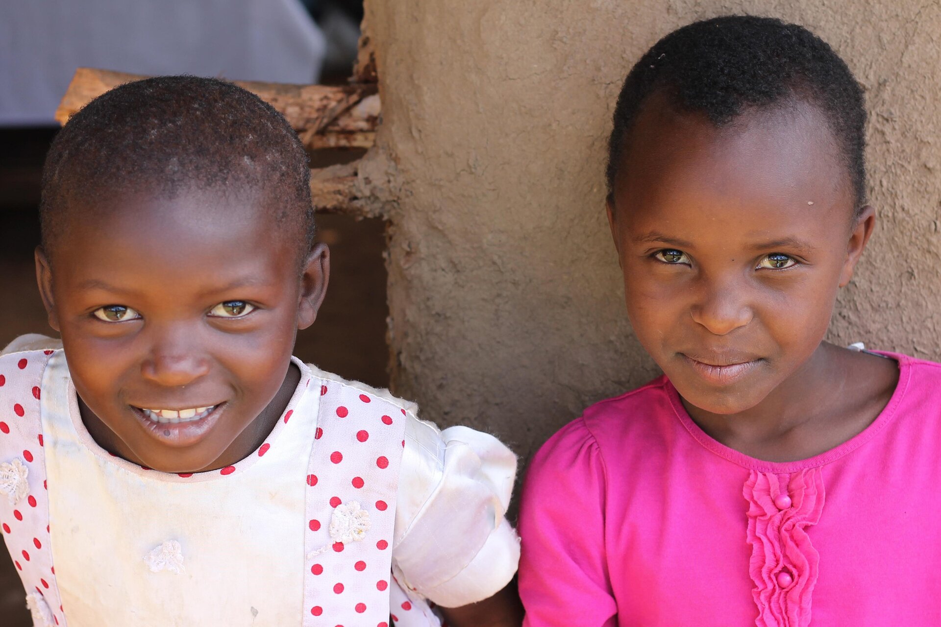 Na zdjęciu widoczne są dwie ciemnoskóre dziewczynki. Dziewczynki mają krótkie, ciemne włosy i brązowe oczy. Uśmiechają się.  