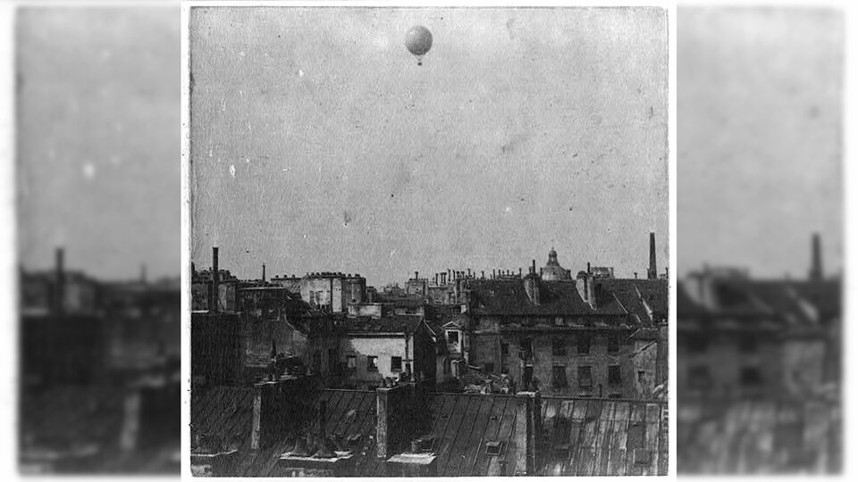 Rysunek przedstawia dachy budynków, nad którymi unosi się lecący balon.