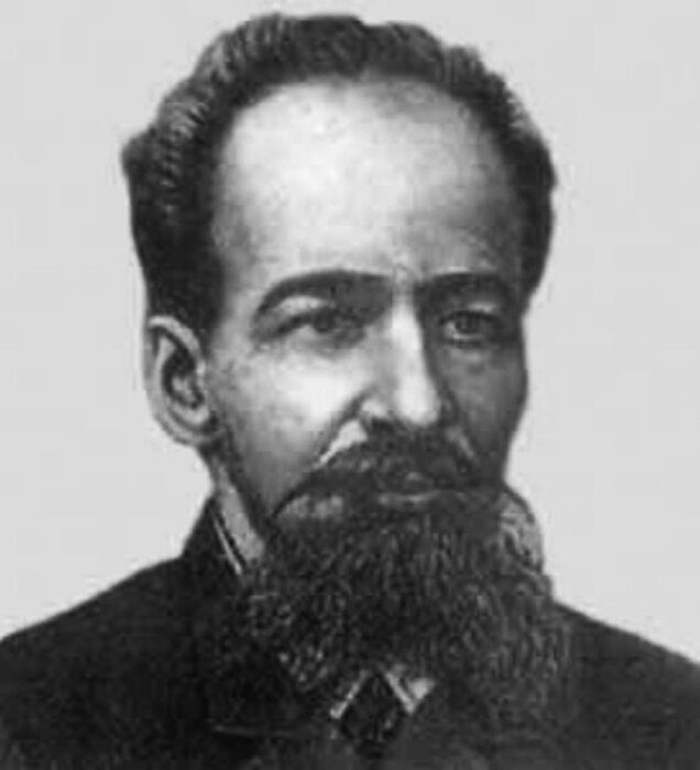 Ilustracja przedstawia portret mężczyzny o szczupłej twarzy, z ciemną brodą i wąsami, wydatnym prostym nosem, dużymi oczami i wyraźnie zaznaczonymi brwiami. Mężczyzna ma wysokie czoło, ciemne włosy zaczesane do tyłu. Jest ubrany w ciemną marynarkę.