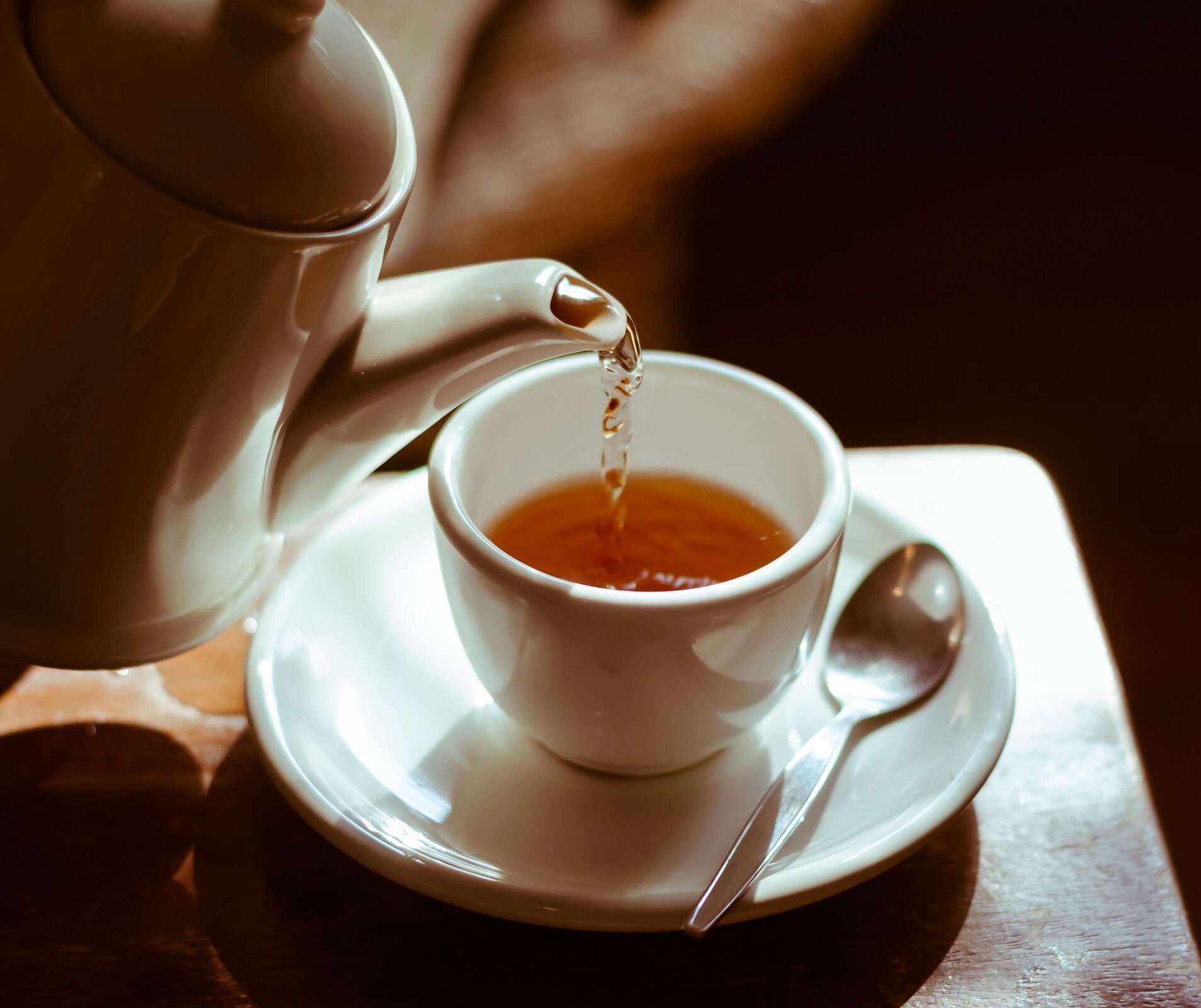 Rys. 2. Zdjęcie przedstawia filiżankę z odrobiną esencji herbaty i pochylonym nad nią imbryczkiem nalewającym gorącą wodę. Filiżanka stoi na talerzyku z łyżeczką.