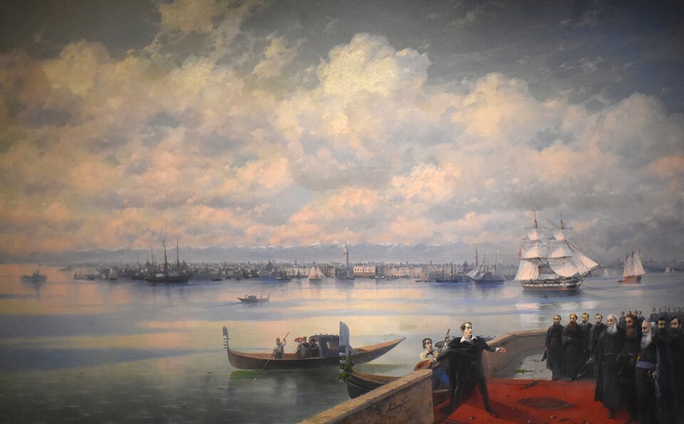 Obraz prezentuje krajobraz morski. Na portowym wybrzeżu znajduje się grupa ludzi. Przypatrują się spokojnemu morzu, po którym pływają łodzie i żaglowce.