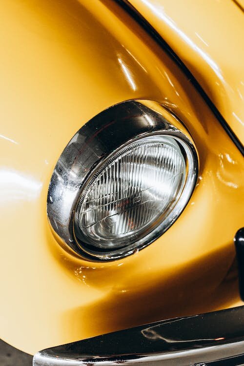 Zdjęcie przedstawiające reflektor świetlny żółtego samochodu. Reflektor ma kulisty kształt.