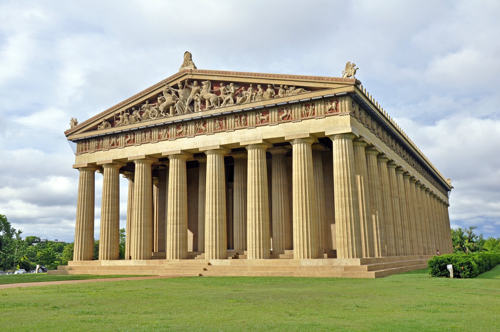 Fotografia przedstawia replikę Partenonu. Konstrukcja budynku jest podparta na kolumnadzie, od frontu na dwóch rzędach. Na tympanonie i fryzie rozmieszczono płaskorzeźby z wizerunkami półnagich ludzi - kobiet w sukniach, mężczyzn w orężu. W narożnikach dachu znajdują się kamienne rzeźby sfinksów. Do budynku prowadzą trzystopniowe schody na całej szerokości budynku, z każdej jego strony. Budynek stoi na zielonym wzgórzu.