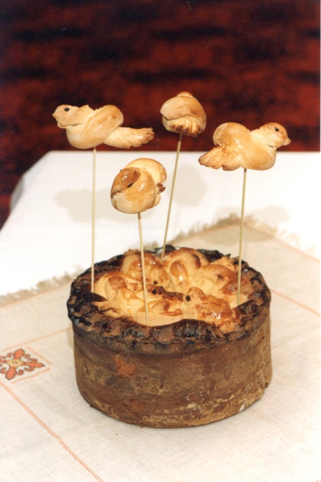 Na zdjęciu tradycyjna potrawa ludowa. Jest to ciasto ozdobione ptaszkami zrobionymi z ciasta chlebowego. Ptaszki zamieszczone są na wykałaczkach, które wetknięte są w drożdżowy torcik. 