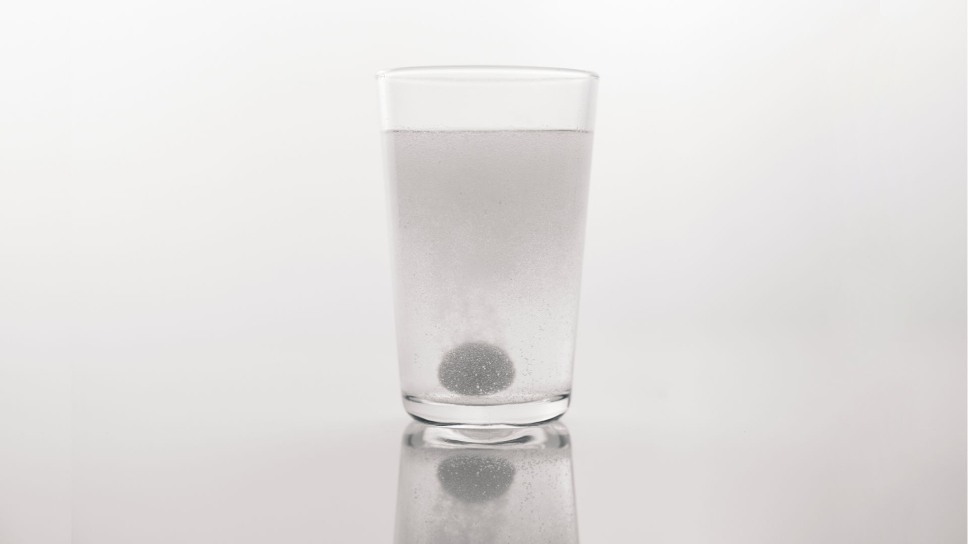 Zdjęcie przedstawia musująca tabletkę rozpuszczającą się w szklance wody.