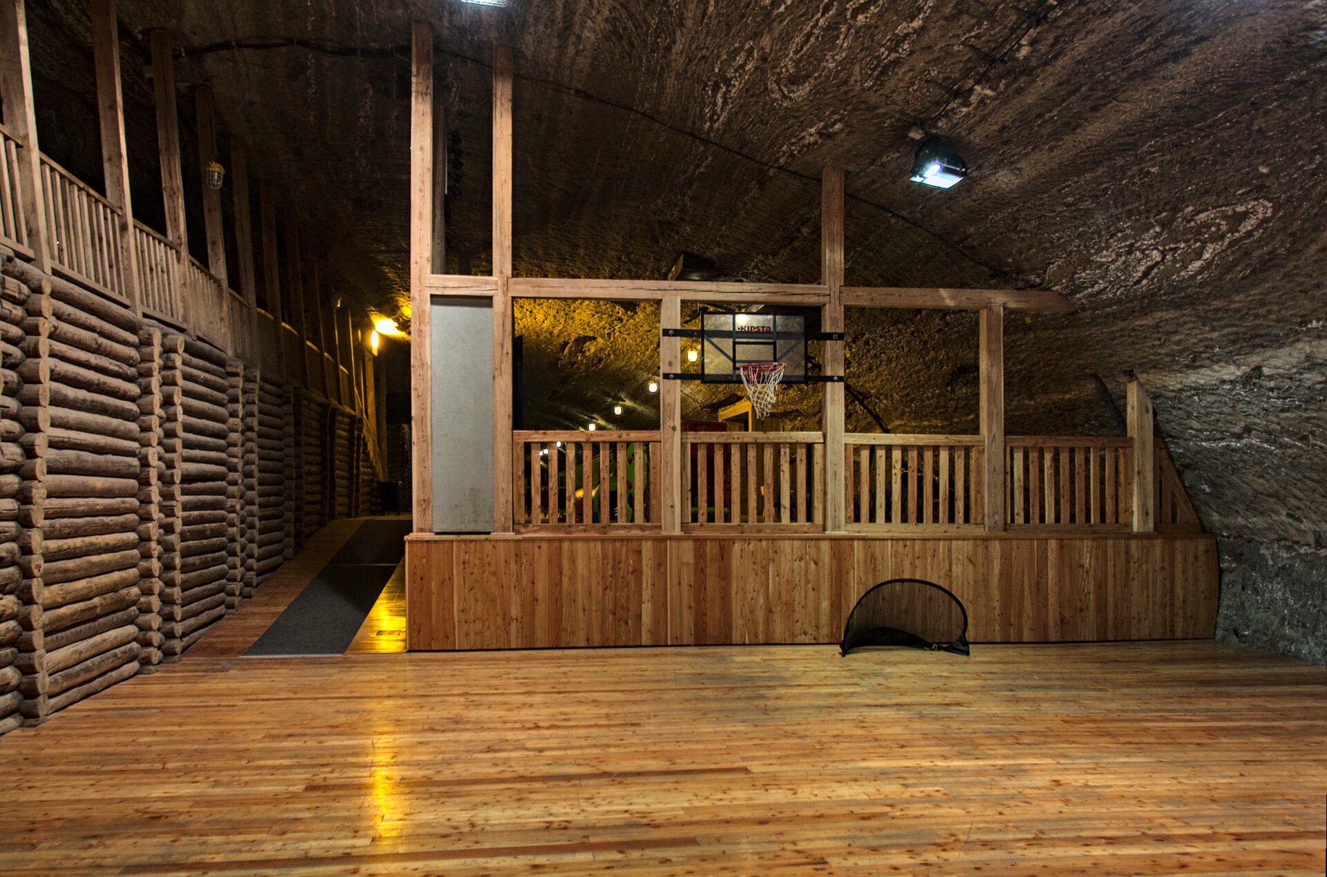 Zdjęcie ukazuje Komorę Ważyn - część sportową. Na zdjęciu znajduje się - za drewnianym ogrodzeniem - kosz do gry w koszykówkę. Strop pomieszczenia jest półokrągły. Podłoga jest drewniana.