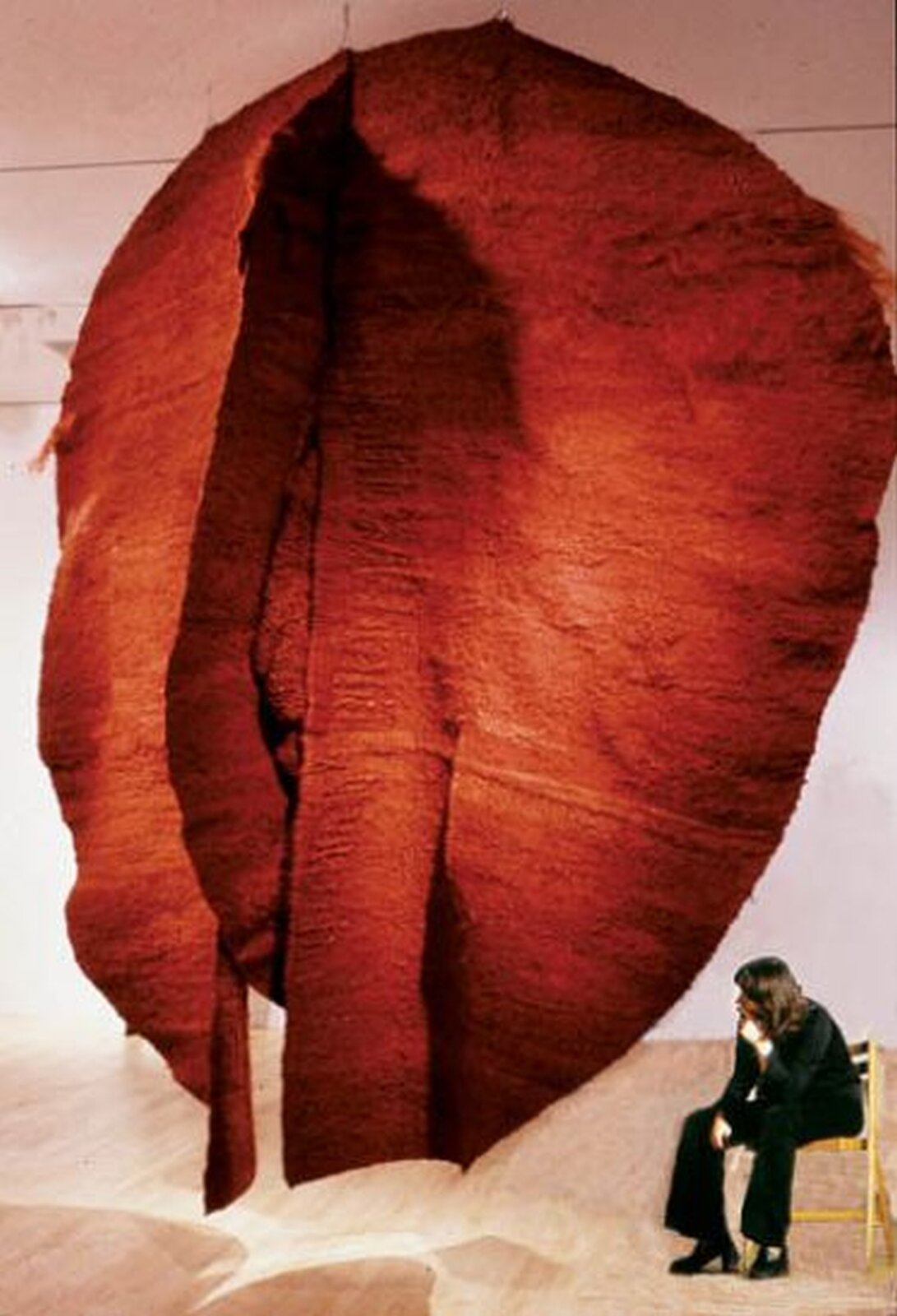 Ilustracja przedstawia dużą płachtę czerwonego materiału. Jest to instalacja artystyczna Abakan czerwony Magdaleny Abakanowicz.