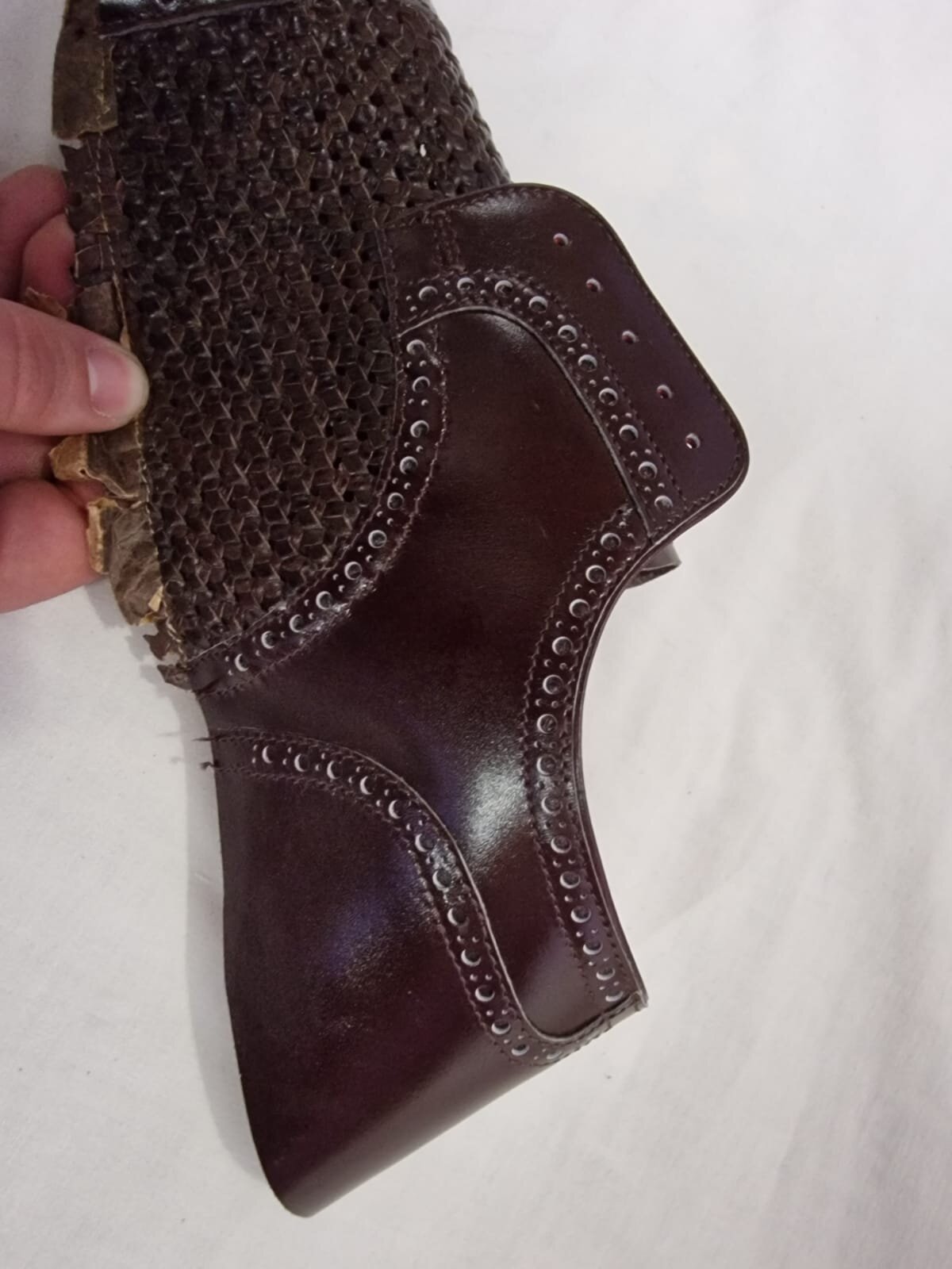 Zdjęcie przedstawia brązowy skórzany kawałek materiału. Jedna jego część jest dziurkowana, a druga siatkowana.