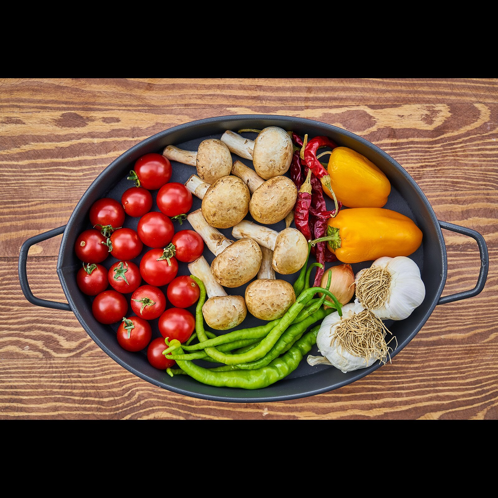 Zdjęcie zrobiono z góry i przedstawia garnek, w którym widoczne są pomidory, pieczarki, papryki, cebulę i czosnek. Pod zdjęciem transkrypcja [odtwórz] 