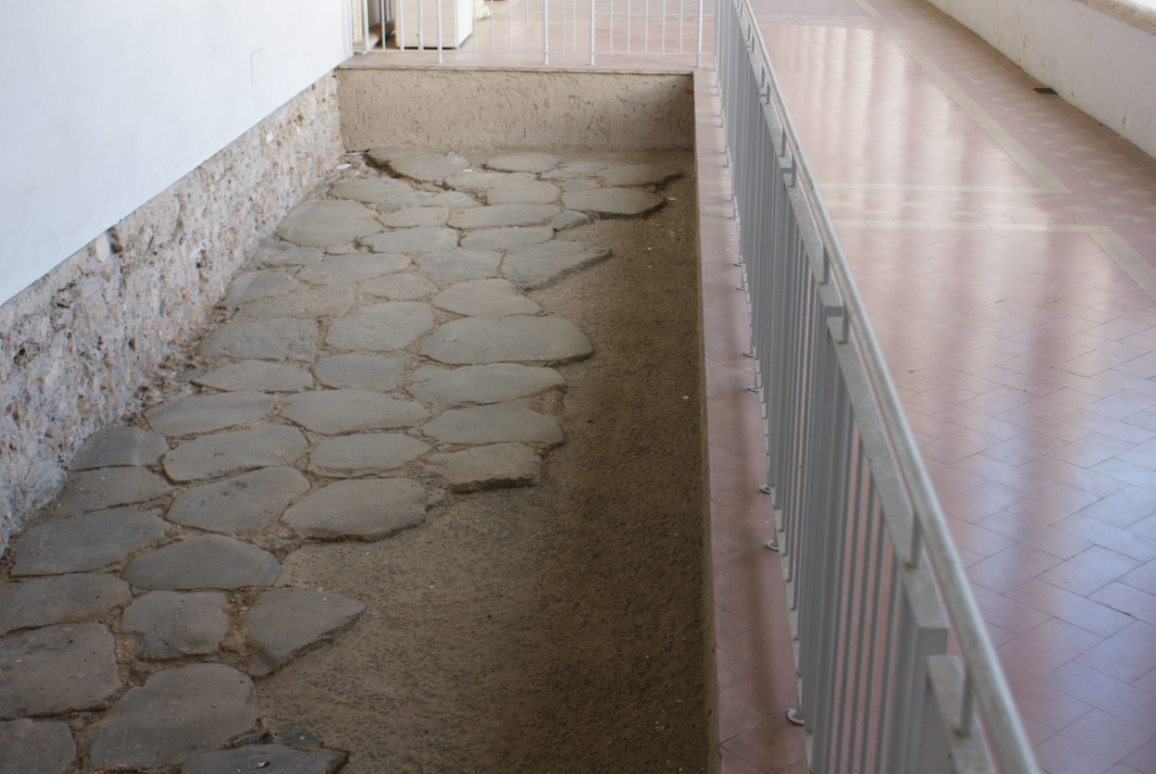 Na zdjęciu zaprezentowany został fragment rzymskiej ulicy, który składa się z płaskich, równo ułożonych kamieni. Fragment ten znajduje się w budynku i został zabezpieczony białymi barierkami.