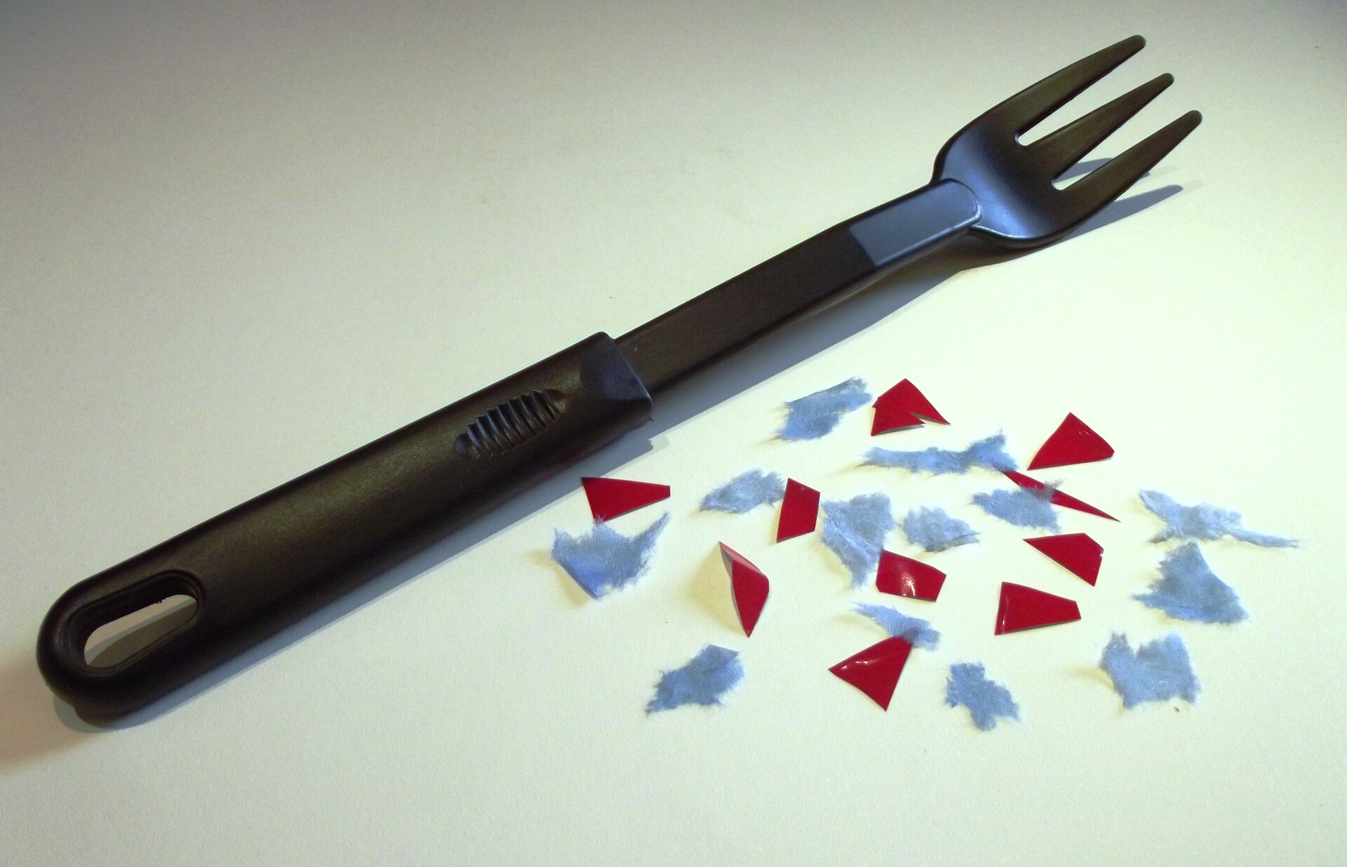 Rys. 7a przedstawia leżący widelec, po prawej stronie widelca leżą skrawki serwetki (błękitne) i cienkiej folii aluminiowej (czerwone).