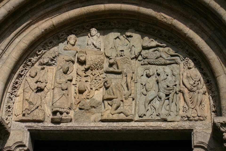  Zdjęcie przedstawia tympan z Bramy Złotników Katedry w Santiago de Compostela. Ma on półokrągły kształt, na jego górnej krawędzi widoczna jest płaskorzeźba z motywami roślinnymi. Pośrodku tympanonu widoczne są liczne płaskorzeźby przedstawiające postacie ludzkie, zwierzęce oraz motywy roślinne. 