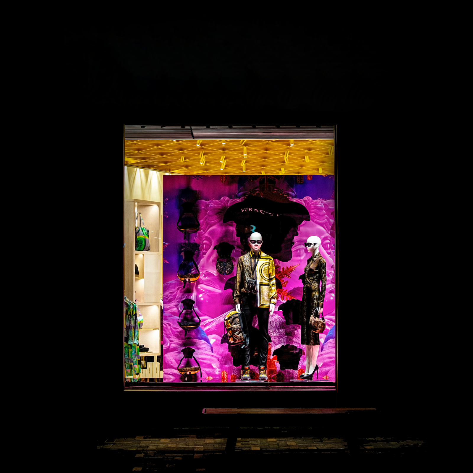 Zdjęcie przedstawia manekiny kobiety i mężczyzny stojące na wystawie sklepu odzieżowego. Widoczna jest nazwa sklepu to Versace. 