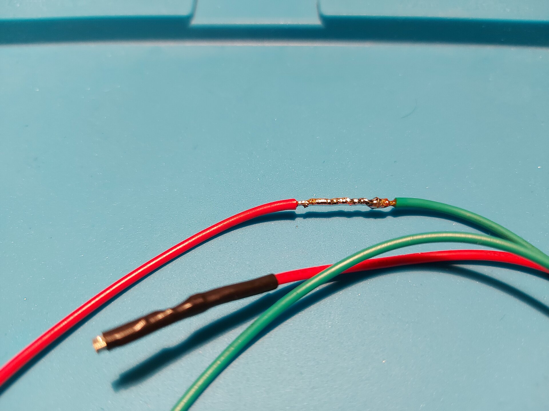 Zdjęcie przedstawia 2 przewody z usuniętą izolacją tym samym odsłaniając miedziane wnętrze, które skręcono ze sobą ustawiając miedziane zakończenia końcami przeciwnymi u podstawy następnego kabla, a następnie zlutowano.