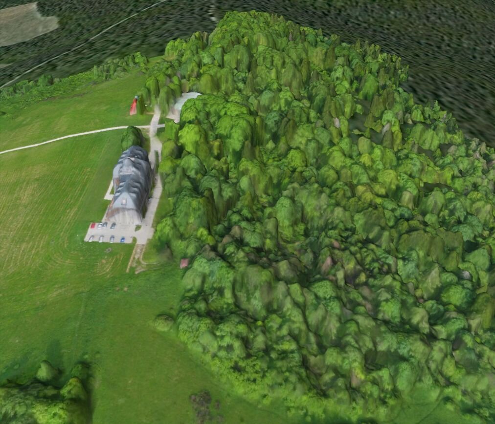 Ilustracja przedstawia widok z góry na teren pagórkowaty, zielony. Na pierwszym planie jest wzniesienie, którego zbocze po prawej stronie jest zalesione, po lewej porośnięte trawą. Na szczycie wzniesienia stoi budynek. Ilustracja powstała wskutek modelowania komputerowego, nosi cechy 3D. Obiekty oddane są za pomocą kształtów o gładkich obrysach.   