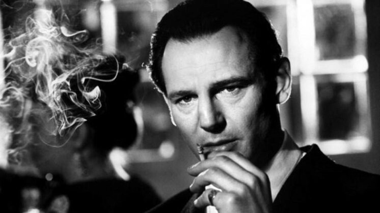 Zdjęcie przedstawia oświetloną w pełni twarz i lewą dłoń mężczyzny. To Schindler. Mężczyzna trzyma w dłoni palącego się papierosa. Na najmniejszym palcu ma sygnet. Przy twarzy mężczyzny unoszą się kłęby papierosowego dymu.