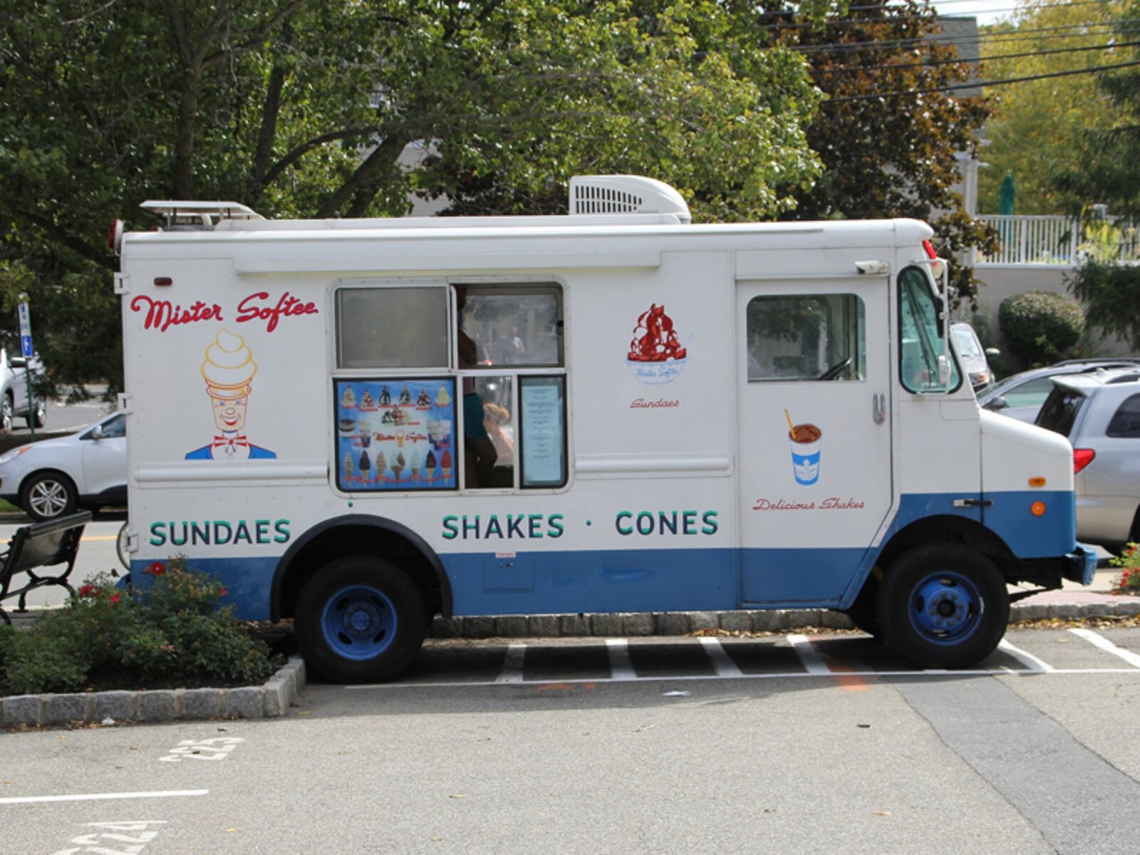 Zdjęcie przedstawia food truck, w którym sprzedawane są lody. Samochód stoi zaparkowany na parkingu.