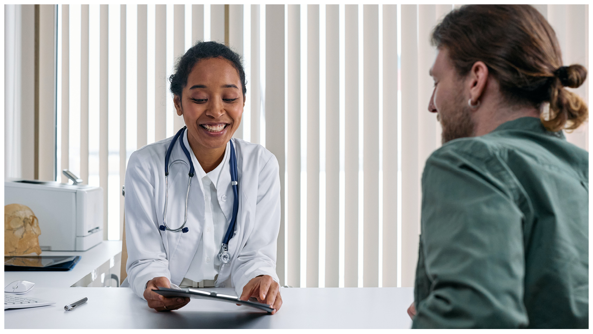 Ilustracja przedstawia uśmiechniętą lekarkę przy biurku, która tłumaczy coś pacjentowi.