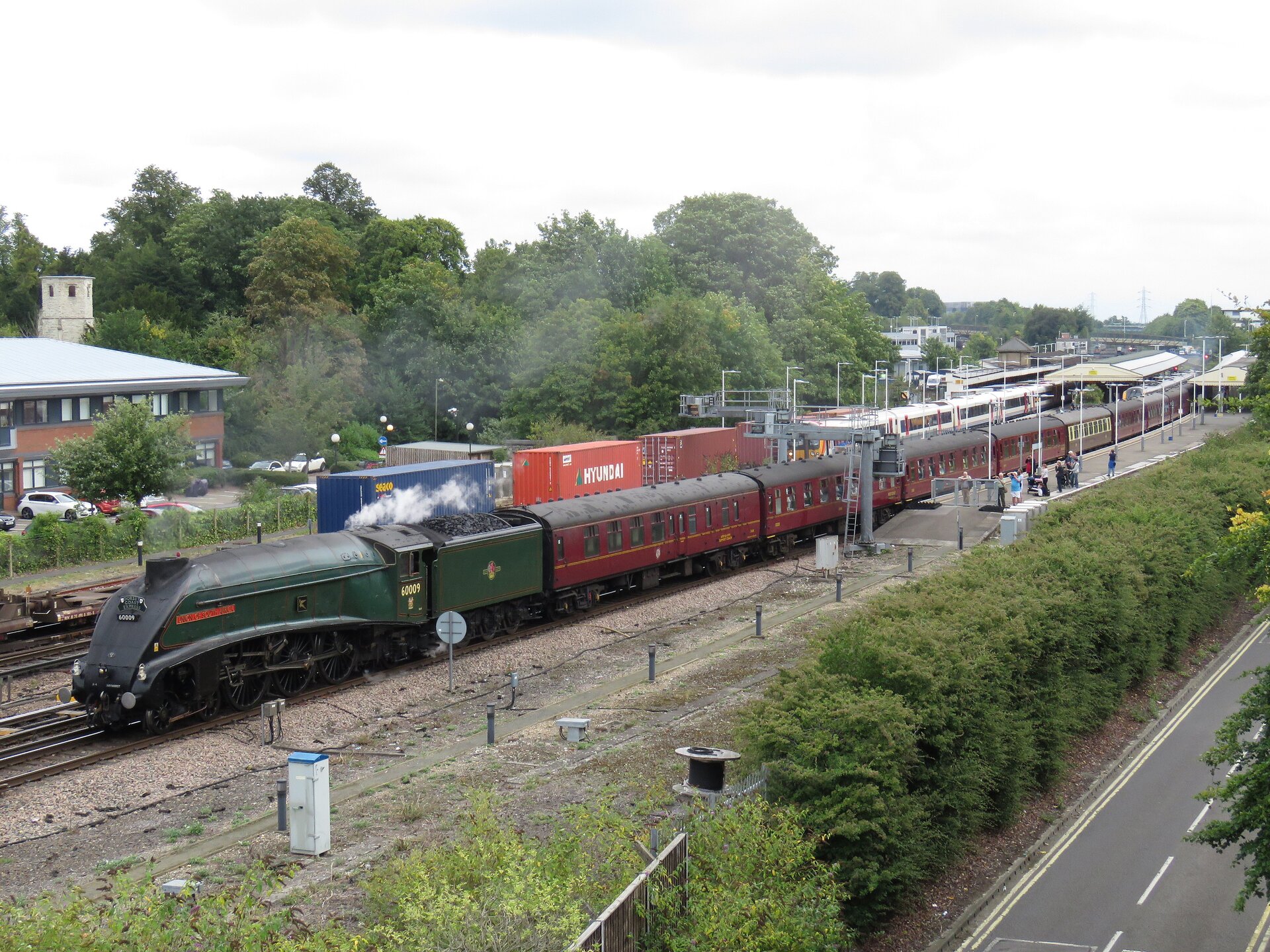 Zdjęcie pociągu pasażerskiego stojącego na peronie. Za lokomotywą znajduje się węglarka. Na torze obok, na drugim planie, kolejny skład.