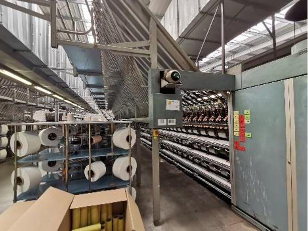 Zdjęcie przedstawia fragment teksturarki. Widoczne są szpule z białymi nićmi zamontowane w maszynie.