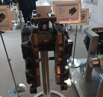 Ilustracja przedstawia zdjęcie zacisku hamulcowego firmy Yujin Machinery eL Te De, wraz z okładzinami hamulcowymi. Grafika pokazuje umiejscowienie dwóch okładzin ciernych – umiejscowione są po wewnętrznej stronie zacisku hamulcowego. Do okładzin ciernych przymocowane są dwa ramiona mające na celu regulowanie siły nacisku.