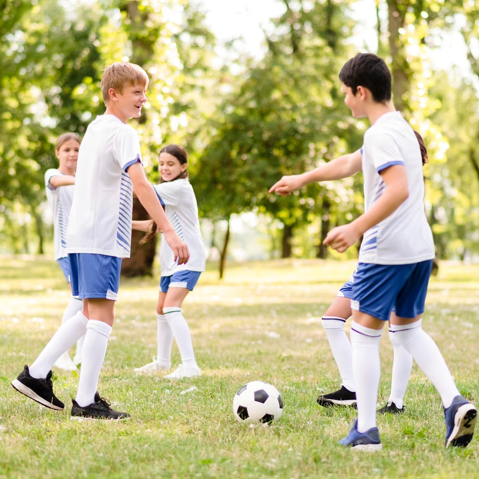 Zdjęcie przedstawia pięcioro dzieci w wieku szkolnym ubranych w strój sportowy, grających w piłkę na trawie. 