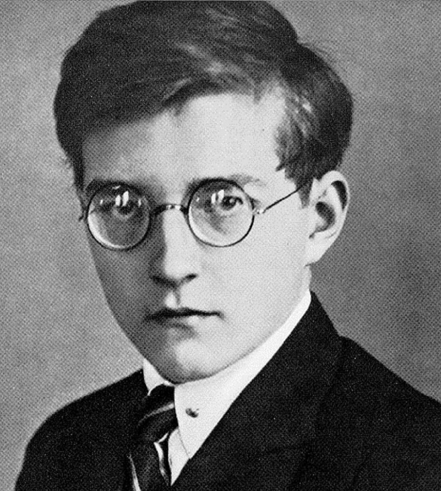 Ilustracja przedstawia Dymitra Szostakowicza jest to rosyjski kompozytor, pianista i pedagog; często uważany był za najwybitniejszego symfonika XX wieku. Mężczyzna w młodym wieku, który nosił okulary. Ma ciemne, gęste włosy, zaczesane na prawą stronę. Ubrany w białą koszulę, krawat i marynarkę.