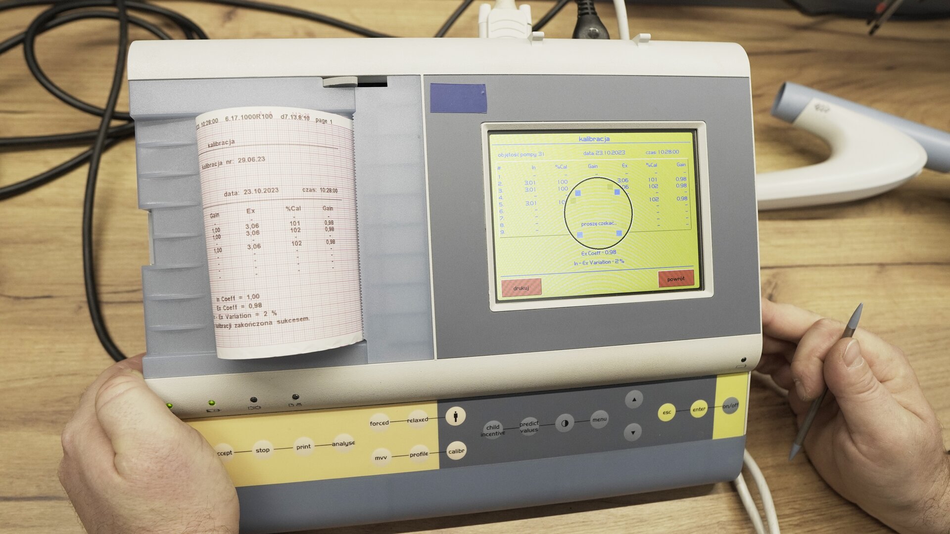 Na zdjęciu pokazano przybliżenie na spirometr. Po prawej stronie aparatu, na ekranie widoczne jest podsumowanie kalibracji, po lewej stronie w drukarce aparatu znajduje się wydruk wyników kalibracji. 