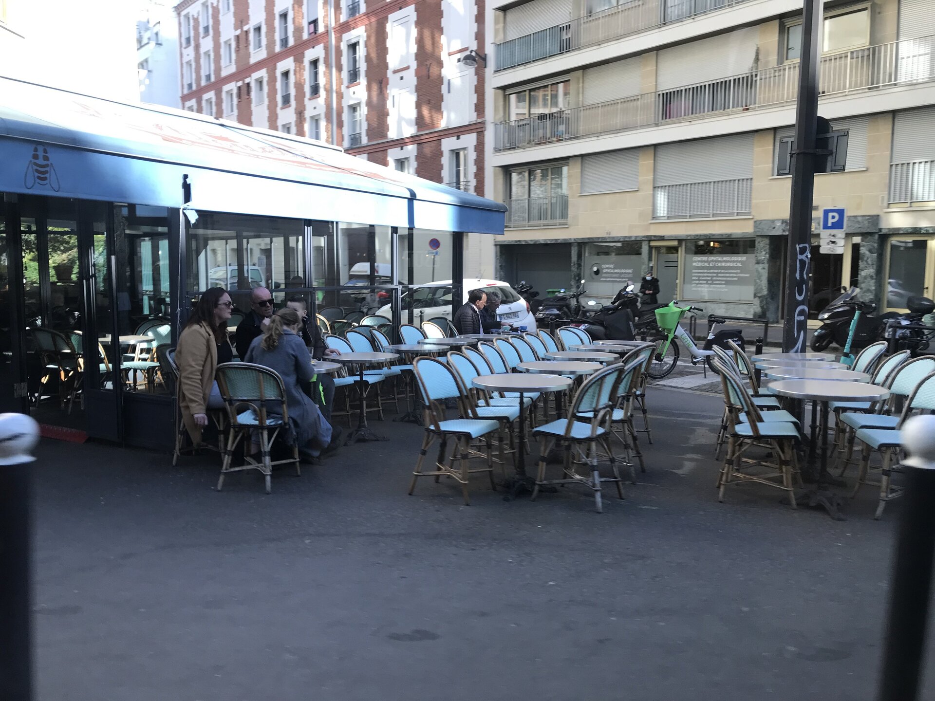 Ilustracja przedstawia stoliki dla klientów ustawione przed restauracją lub kawiarnią.