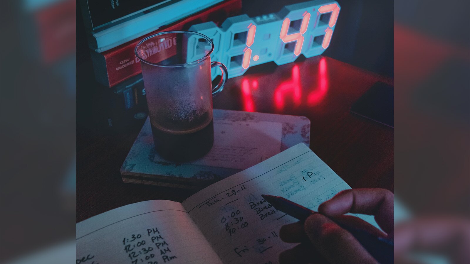 Zdjęcie przedstawia biurko, na którym stoi zegar wskazujący godzinę 1:47, a przed nim znajduje się kubek z ciemnym napojem. Przed kubkiem leży notes, na którym ktoś trzyma prawą dłoń z długopisem. Transkrypcja nagrań znajduje się poniżej.