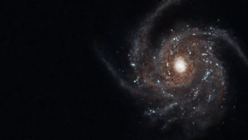 Na czarnym tle kosmosu widać dużą galaktykę spiralną. Po prawej stronie obrazu znajduje się jasne, niemal białe centrum galaktyki, otoczone spiralnymi ramionami w odcieniach brązu, szarości i delikatnego błękitu. W ramionach widoczne są liczne drobne, jasne punkty – skupiska gwiazd. Spiralna struktura stopniowo zanika w ciemności przestrzeni kosmicznej po lewej stronie obrazu. Całość sprawia wrażenie wirującego świetlnego dysku zawieszonego w ogromnej, ciemnej pustce.