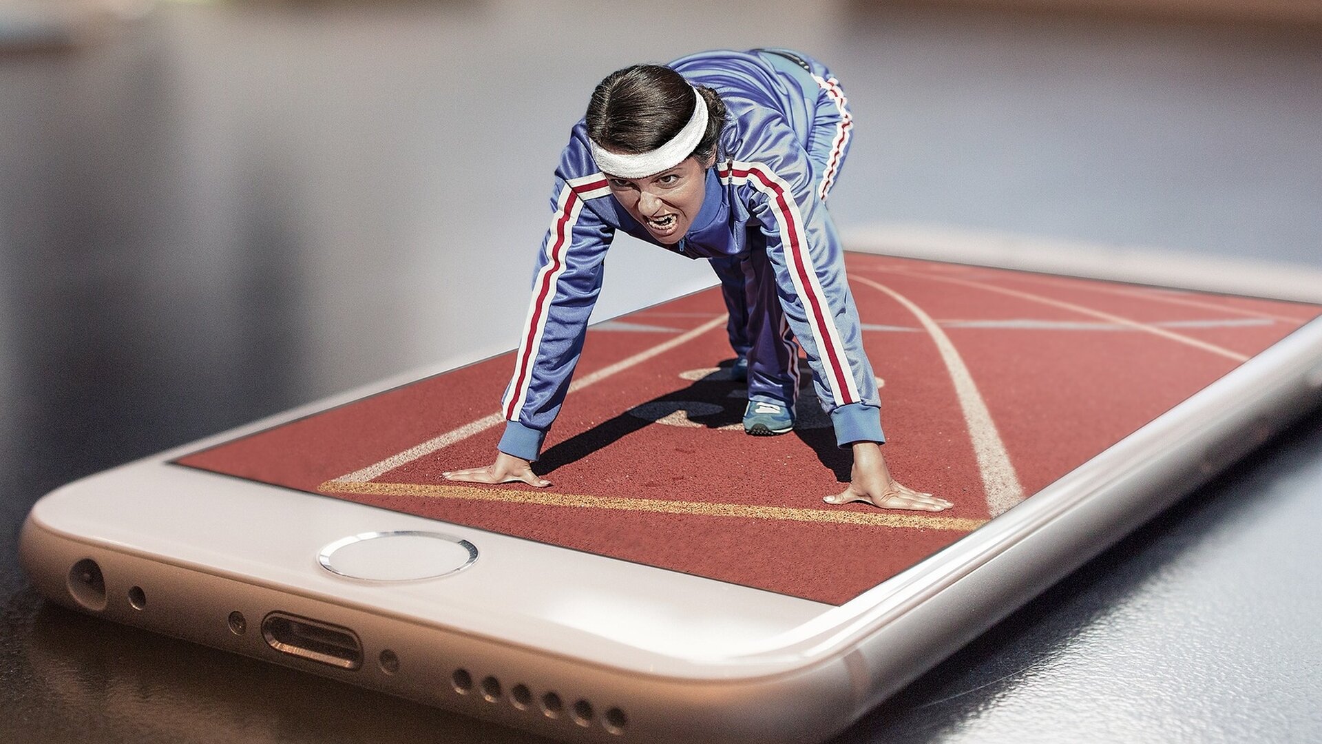 Ilustracja to fotomontaż przedstawiający kobietę startującą do biegu z wyświetlacza telefonu komórkowego, na którym widać bieżnię na stadionie. Kobieta ubrana jest w dres z długim rękawem, włosy ma zebrane opaską. Stoi w pozycji startowej z miną pełną determinacji.