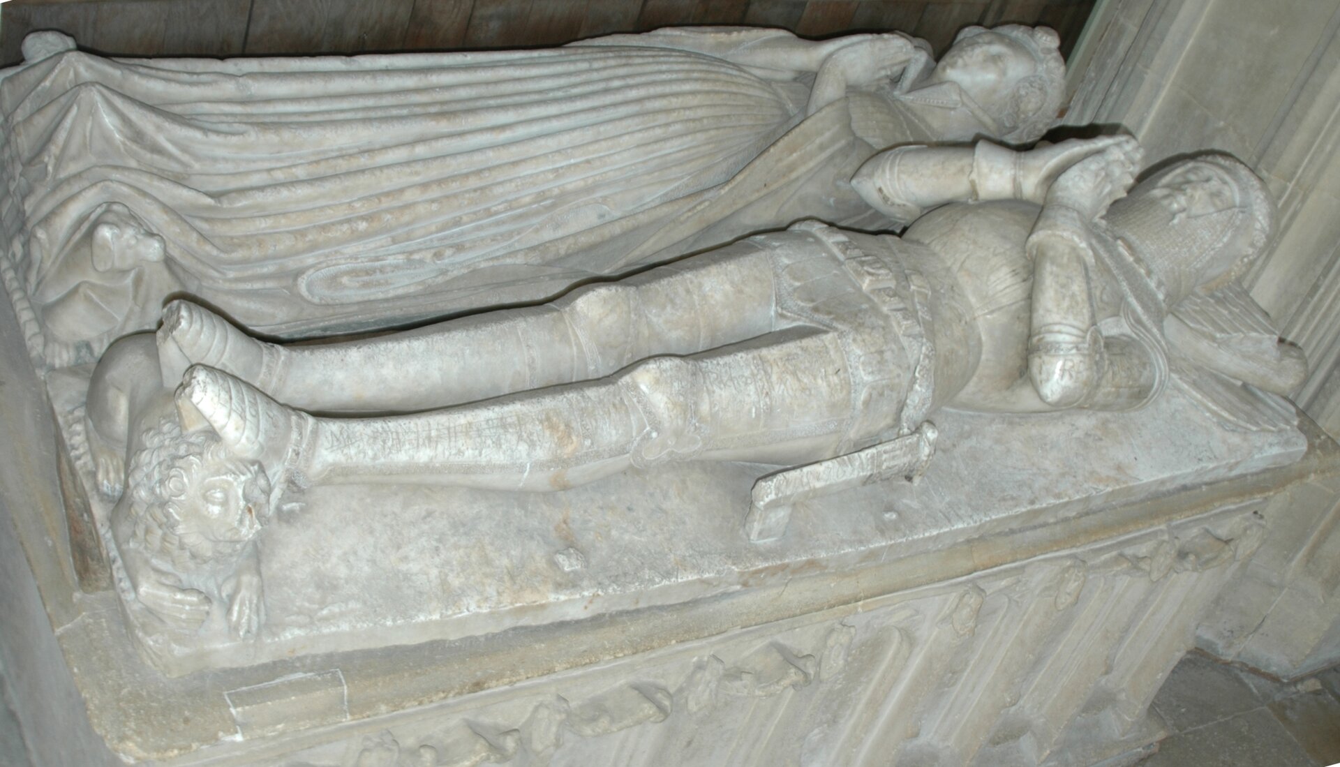 Na zdjęciu jest grobowiec wykonany z jasnego materiału. Powierzchnie grobowca stanowią dwie leżące sylwetki - mężczyzny i kobiety. Mają dłonie złożone do modlitwy.