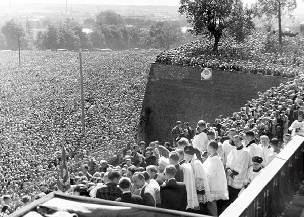 Zdjęcie przedstawia duchownych odprawiających uroczystość religijną. Znajdują się na wzniesieniu. Na dole jest się tłum ludzi.