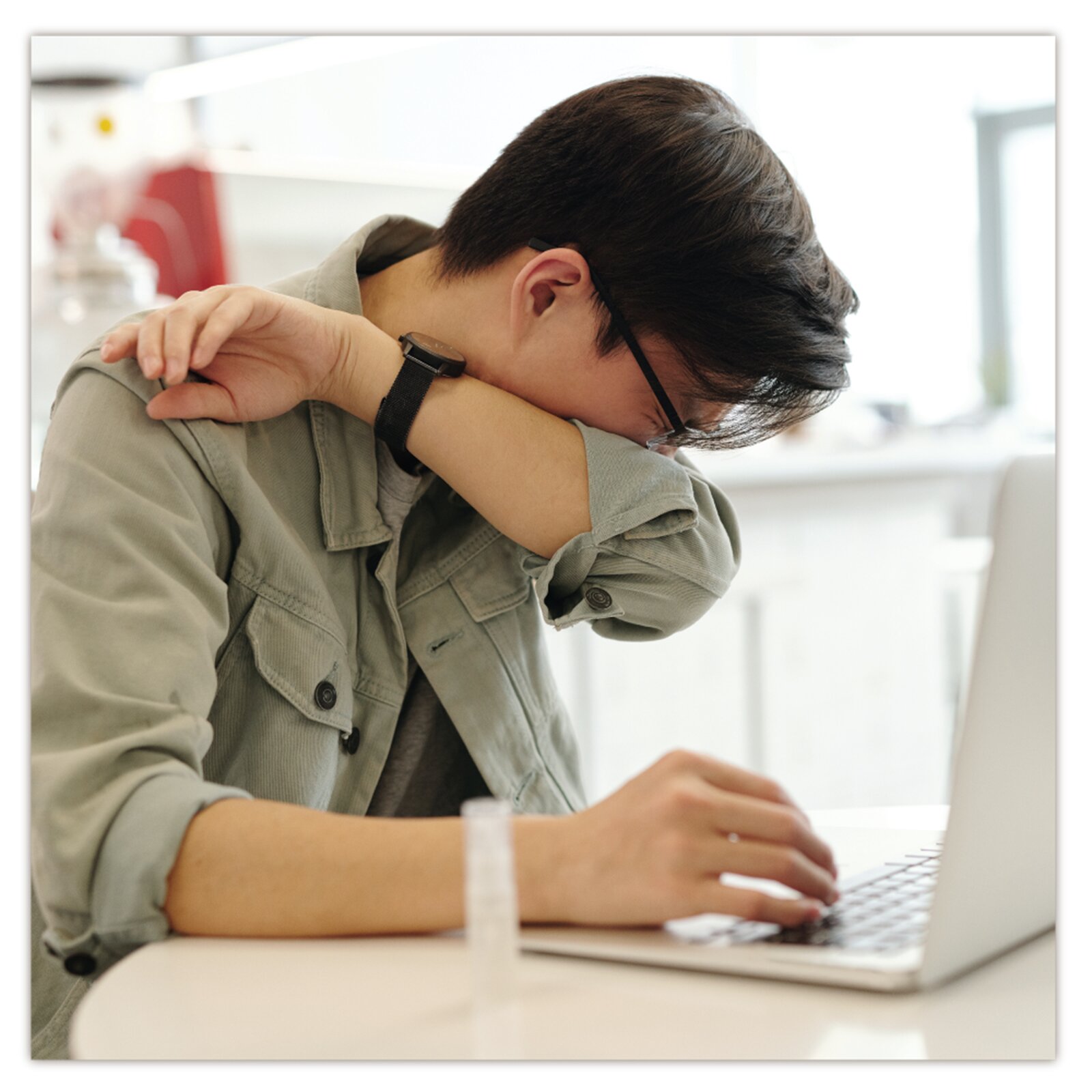 Na zdjęciu widoczny jest siedzący przy komputerze chłopak, który kicha. 