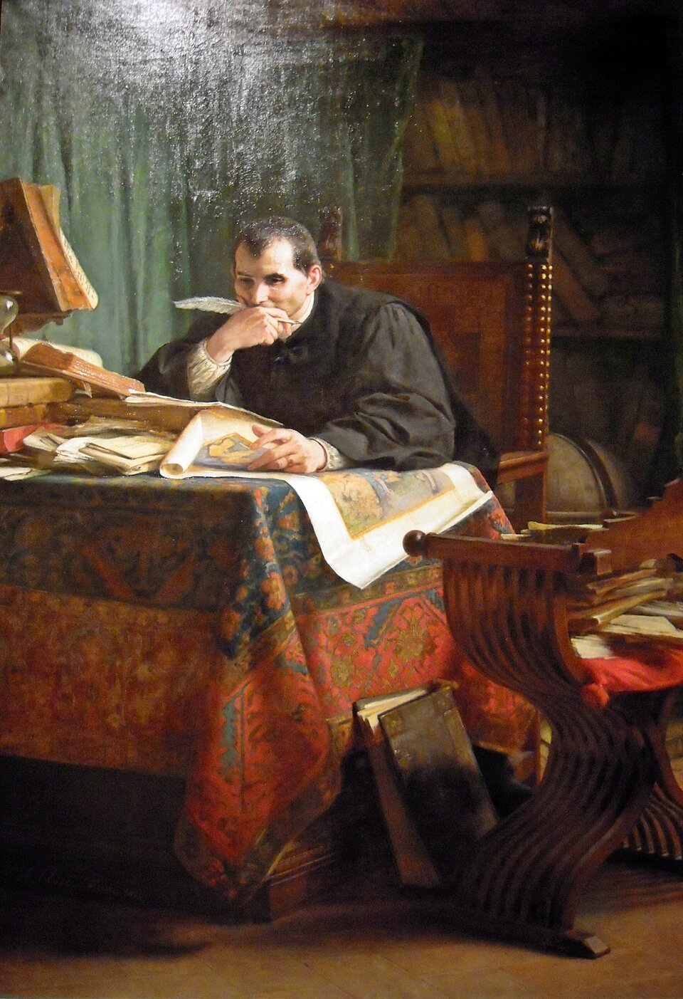 Obraz „ Niccolò Machiavelli w swoim gabinecie” to realistyczny, niezwykle nastrojowy portret myśliciela, historyka i pisarza epoki renesansu. W centrum kadru siedzi Niccolò Machiavelli , przedstawiony jako dojrzały, głęboko skupiony mężczyzna o krótkich włosach. Prawą ręką wspiera brodę, a w ustach trzyma gęsie pióro, jakby na chwilę przerwał pisanie, aby przeanalizować skomplikowany problem polityczny. Druga ręka spoczywa na rozłożonym dokumencie. Mężczyzna nosi ciemne, skromne szaty z epoki. Ciemny ubiór kontrastuje z jasnym kolorem papieru i pióra, co skupia wzrok widza bezpośrednio na twarzy i dłoniach bohatera. Wyraz twarzy Machiavellego jest surowy. Gabinet jest ciasny, wypełniony po brzegi księgami i kartkami. Masywny stół, przy którym siedzi pisarz przykryty jest bogato zdobionym, ciężkim obrusem w orientalne, czerwono‑błękitno‑złote wzory. Na stole panuje nieład, piętrzą się na nim sterty starych ksiąg, rozłożone pergaminy, kałamarz oraz duża, kolorowa mapa lub iluminowany manuskrypt. Machiavelli siedzi na rzeźbionym, wysokim krześle. Na pierwszym planie po prawej stronie widoczne jest puste, rzeźbione krzesło bez oparcia o wygiętych nogach, na którym leżą ułożone niedbale dokumenty. Dwie opasłe księgi opierają się o nogę stołu na podłodze. W tle, za plecami pisarza, w półmroku rysują się solidne regały, uginające się pod ciężarem ksiąg. Z prawej strony, za głową filozofa wisi ciężka, zielona kotara. Całość oświetlona jest silnym, punktowym światłem z lewej strony, które rozjaśnia blat roboczy i twarz mężczyzny, pozostawiając resztę gabinetu w tajemniczym cieniu.